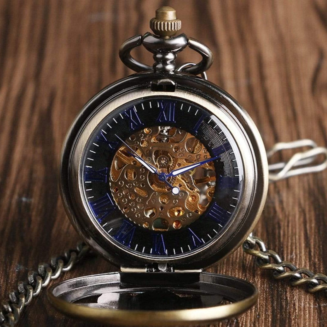 Close-up of a silver-and-gold skeleton pocket watch with a chain, set on a wooden surface.