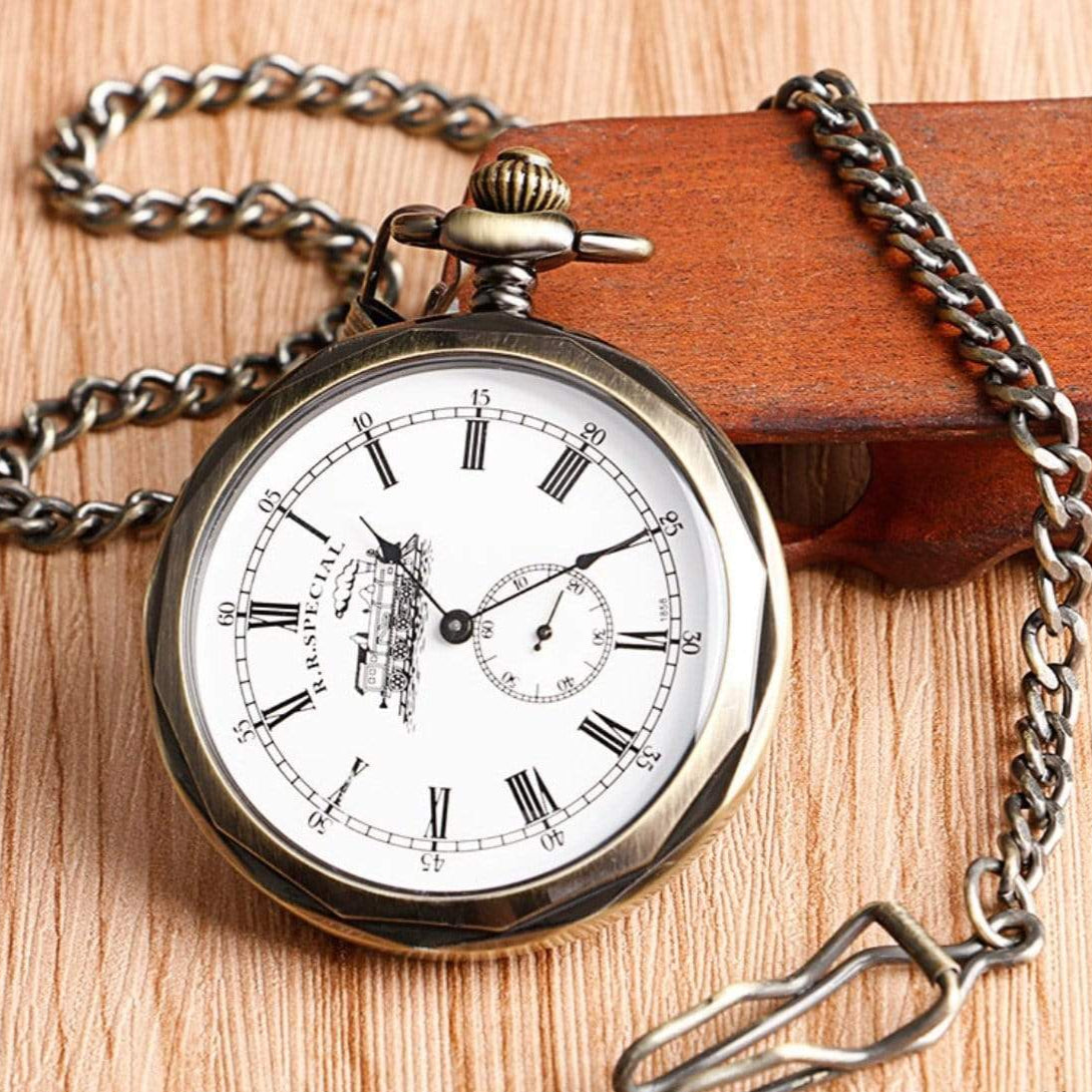 Antique bronze-colored pocket watch with chain on a wooden surface.
