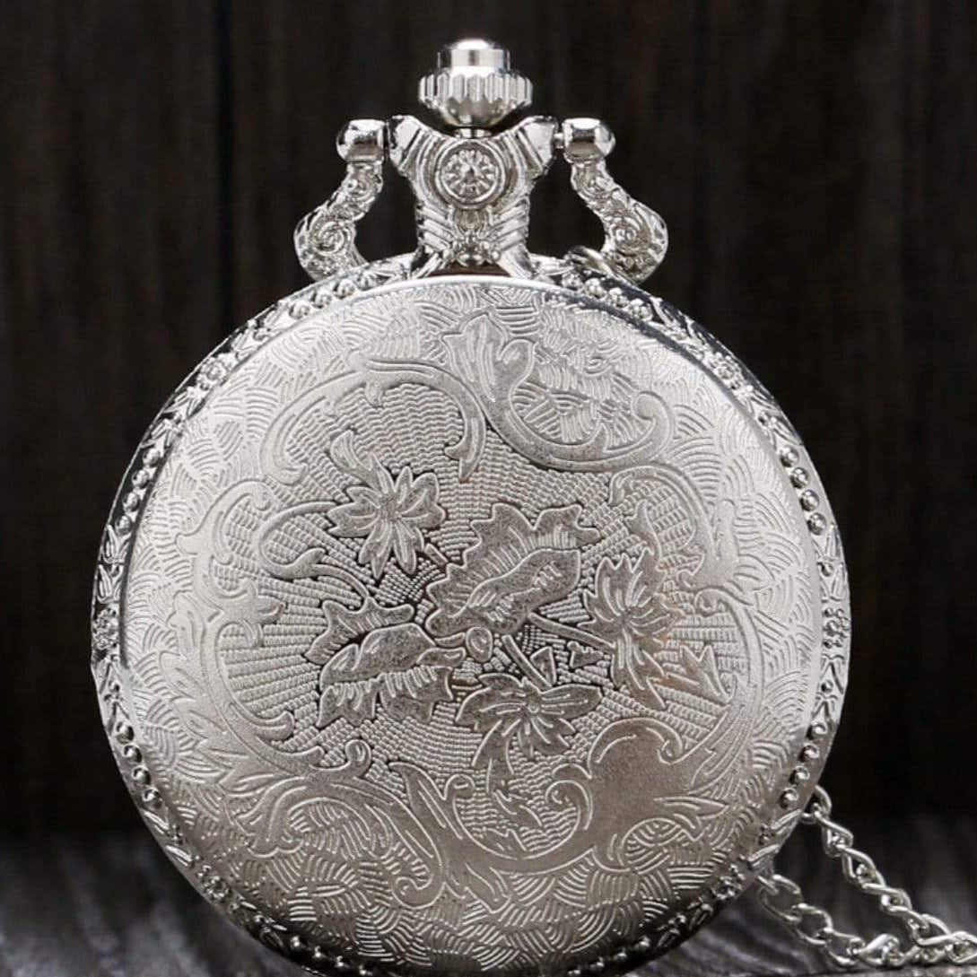 Silver pocket watch with ornate floral design and chain.
