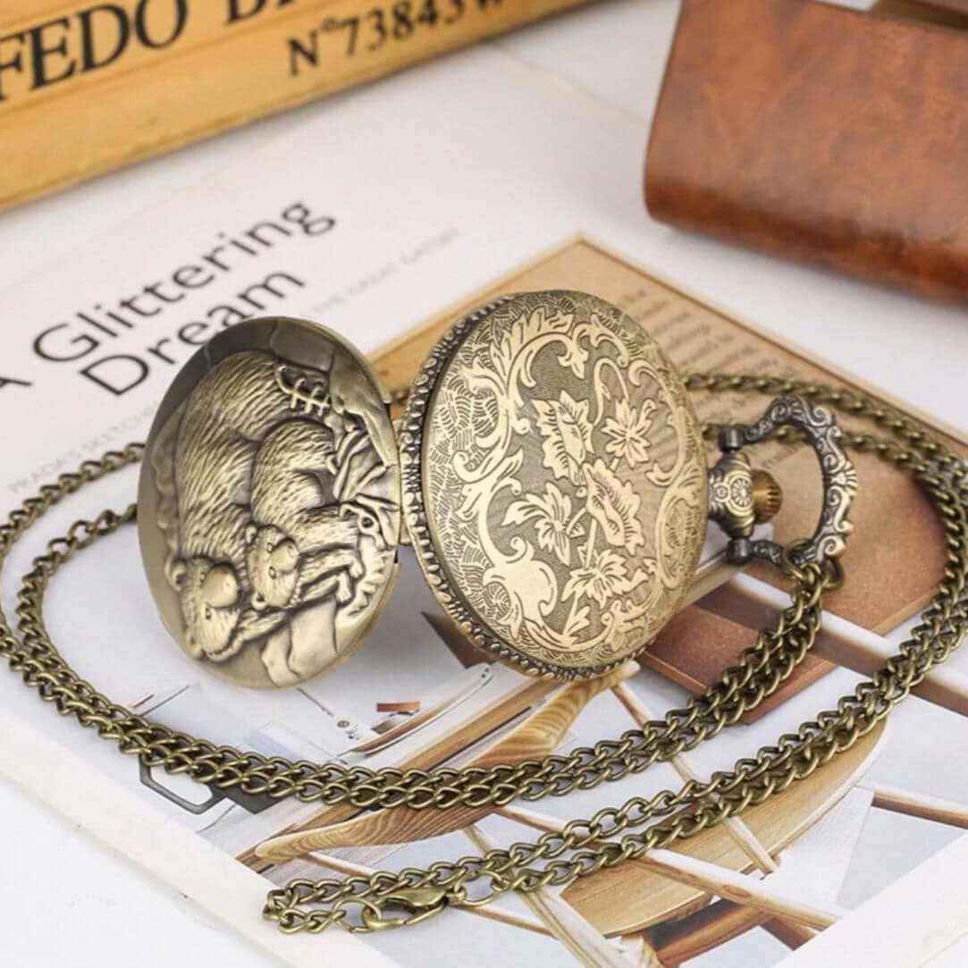 A bronze-colored pendant pocket watch with a chain. The watch has a floral design on one side and a depiction of a mother bear and cub on the other.