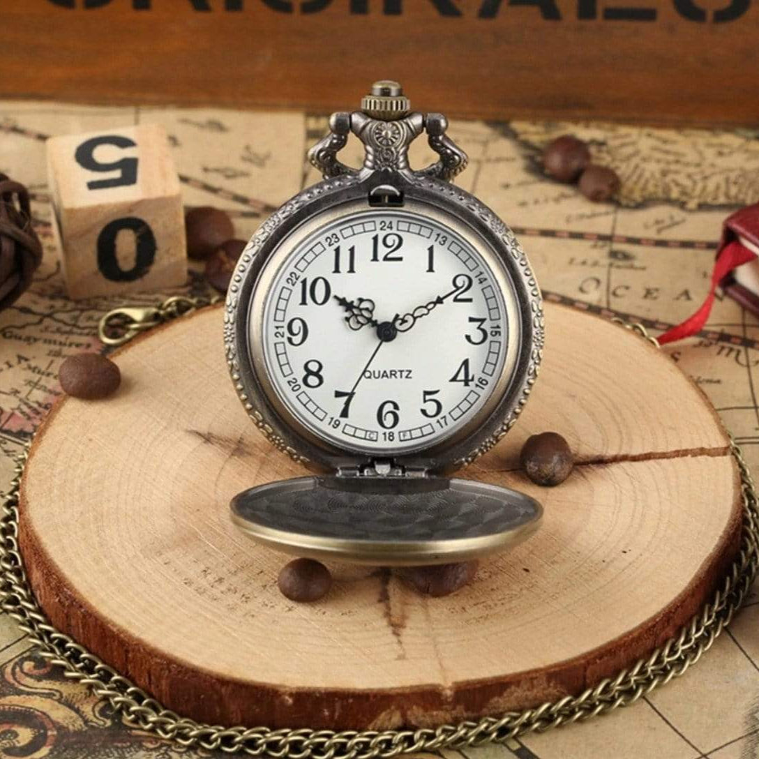 Antique pocket watch with lid open, on a wood slice, surrounded by a chain, with a wooden block and map in the background.
