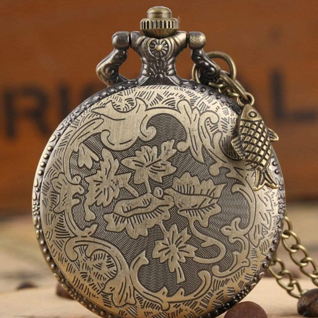 Bronze pocket watch with floral engraving and fish charm.
