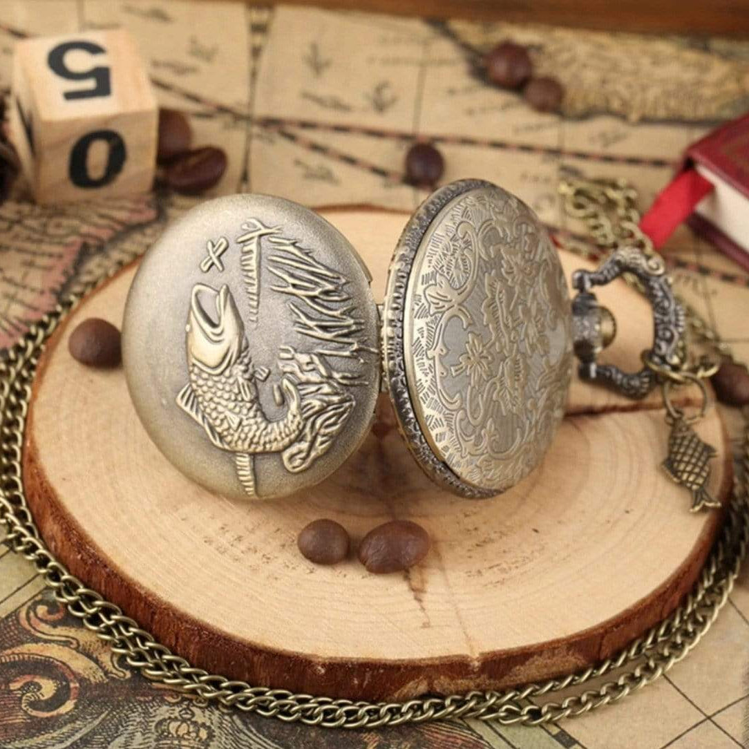 Open pocket watch with fish design on a wooden slice.
