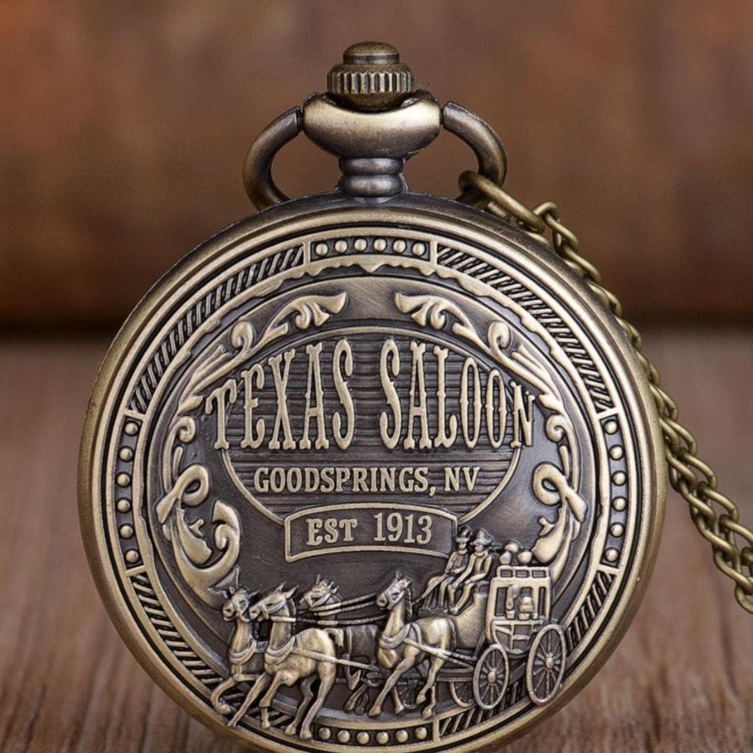 Antique brass pocket watch with "Texas Saloon, Goodsprings, NV, Est 1913" engraving and horse-drawn carriage scene.
