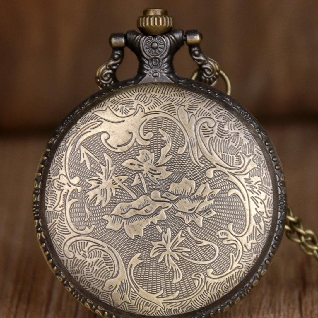 Close-up of an ornate, bronze-colored pocket watch with floral design.
