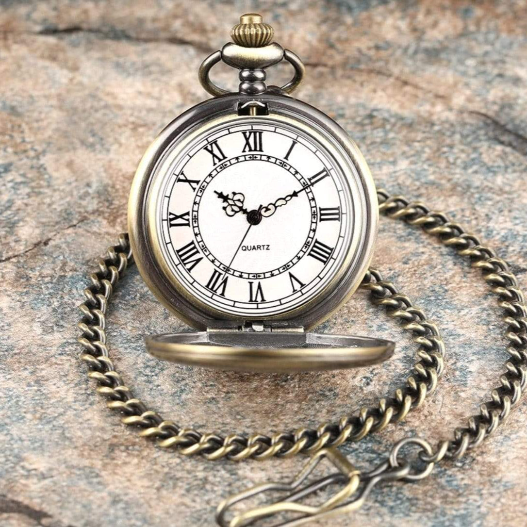 Silver and bronze pocket watch with chain on a textured stone surface.