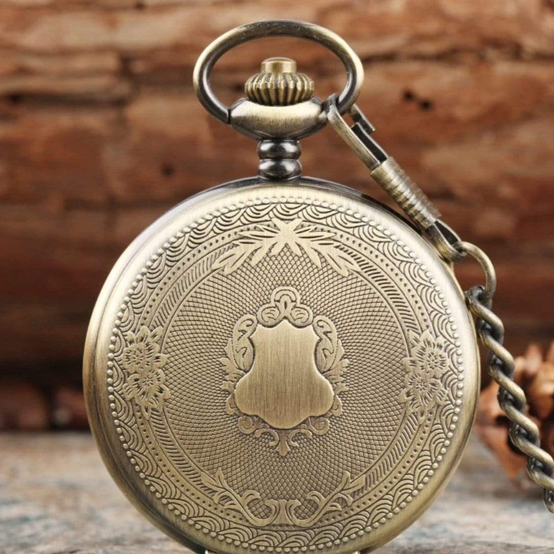 Close-up of an ornate, bronze-colored pocket watch with a chain.
