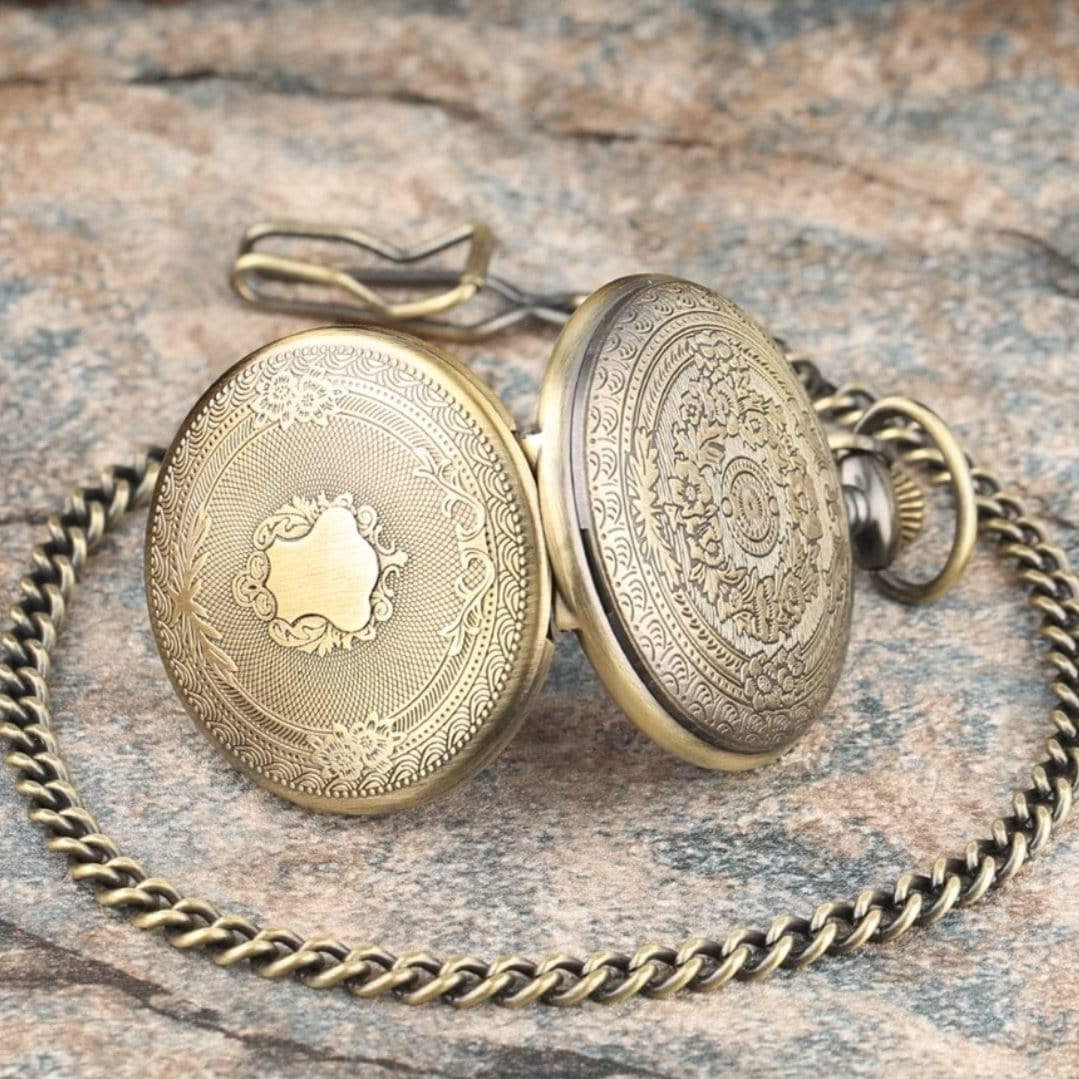 Open bronze pocket watch with chain on stone surface.

