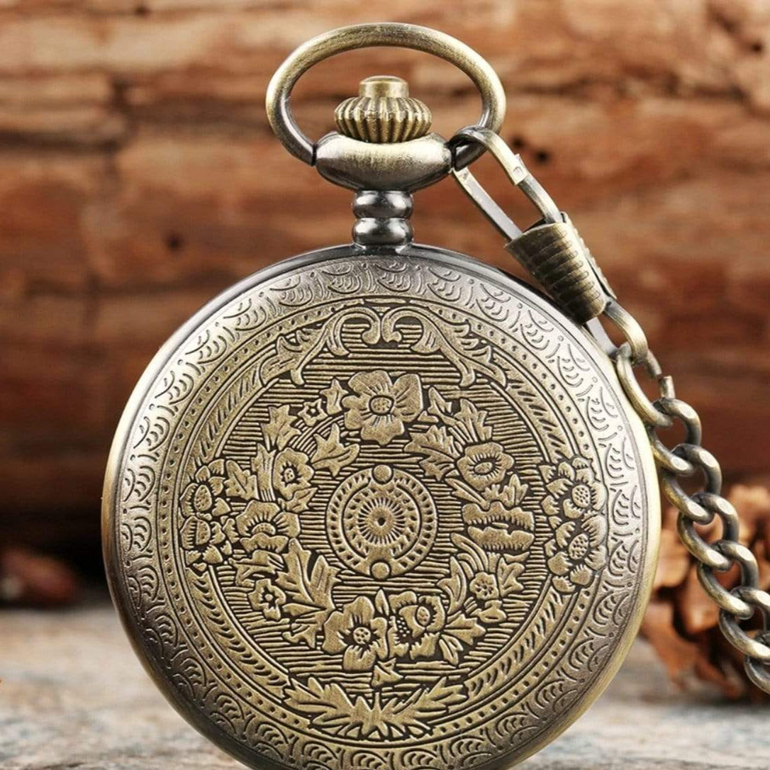 Close-up of a bronze-colored antique pocket watch with floral engravings and chain.