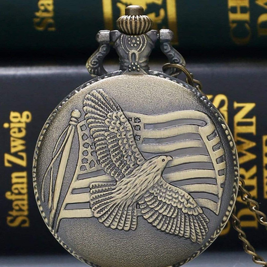 Close-up of a bronze pocket watch featuring an American eagle and flag design, with books in the background.