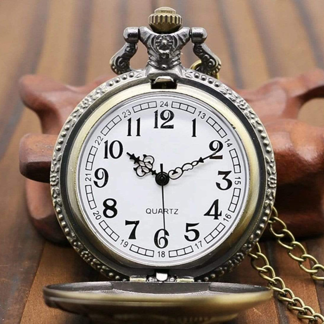 Close-up of an open vintage pocket watch with a white face, black numerals, and a bronze-colored case and chain on a wooden surface.