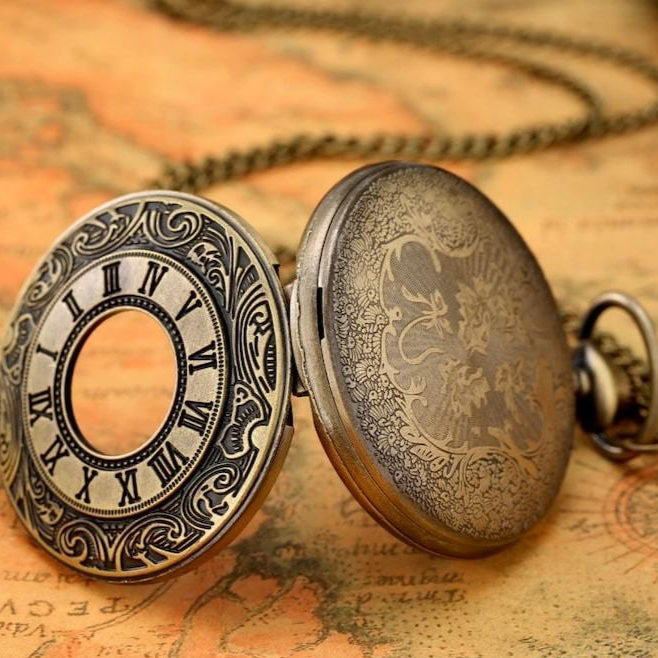 Open, ornate, bronze pocket watch with a chain on a map.
