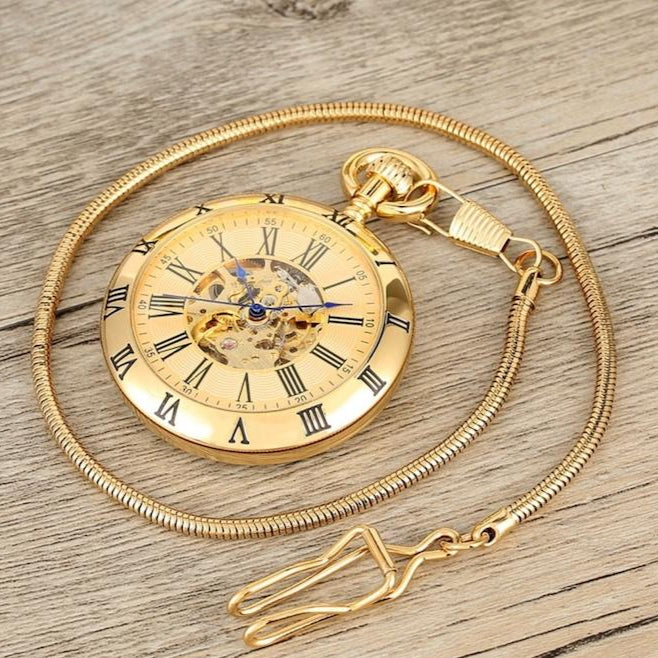 A gold-colored open-face pocket watch with a matching gold chain resting on a wooden surface.
