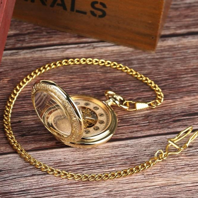 Gold pocket watch with lid open on wood surface.