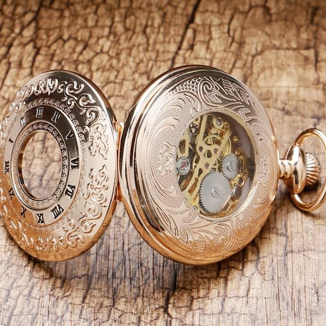 A gold pocket watch with an open face showing gears, displayed on a wooden surface.
