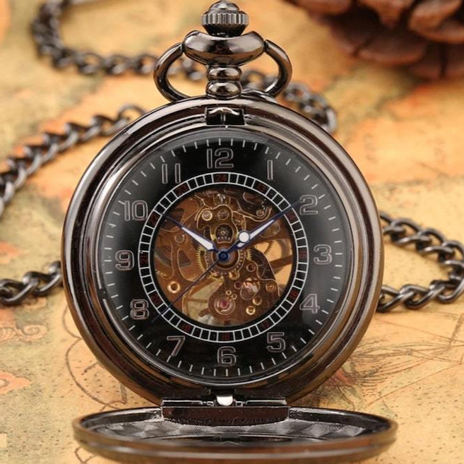 Close-up of a black mechanical pocket watch on a patterned surface with a chain.