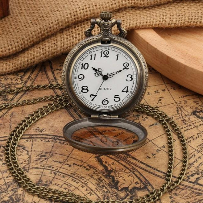 Open silver pocket watch with bronze chain on map surface.
