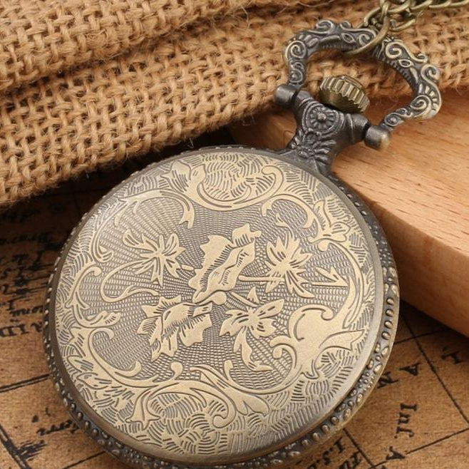 A vintage, brass-colored pocket watch with floral engravings, a decorative handle, and chain, resting on a wooden surface and an old map.