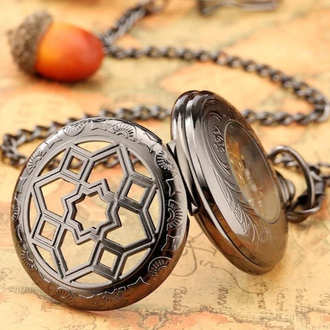 Open black pocket watch with ornate cut-out lid, acorn charm, and chain on map.