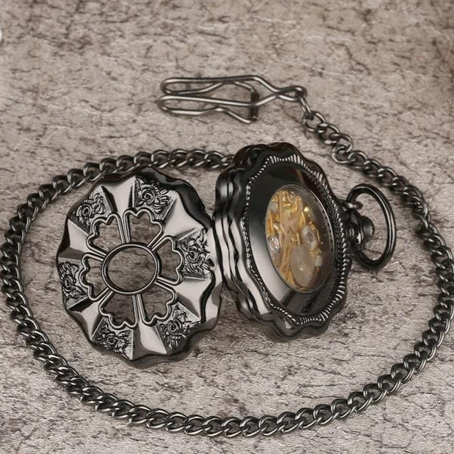 A close-up shot of an open, decorative, black pocket watch with a chain.