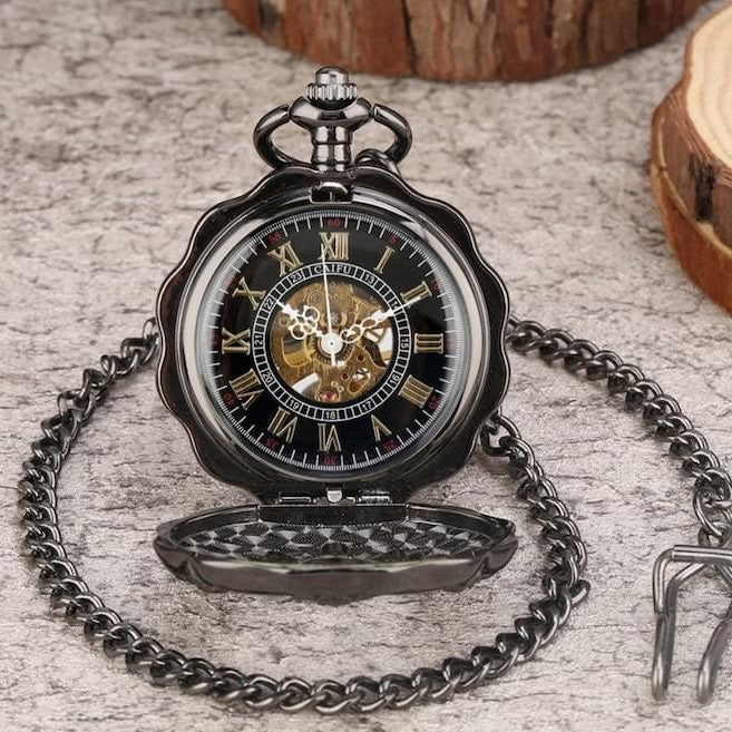 Pocket watch with a black chain on a gray surface.
