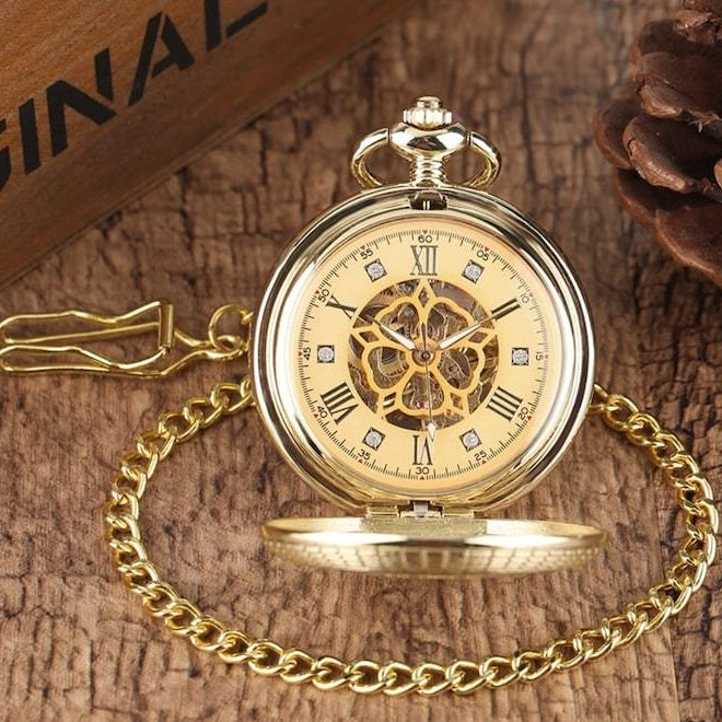 Gold pocket watch with chain on wood surface.
