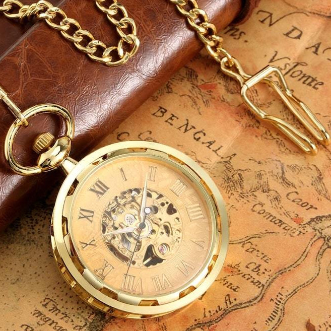 Gold pocket watch with Roman numerals, a gold chain, and a brown notebook on an antique map.