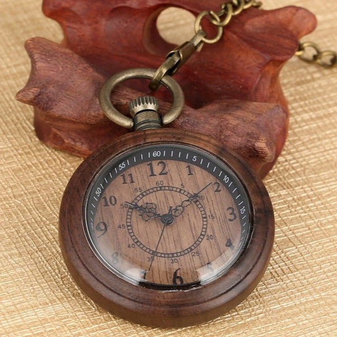 Close-up of a wooden pocket watch with a bronze chain, resting on a wooden surface.