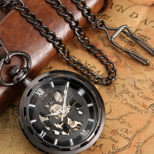 Close-up of a black skeleton pocket watch with a matching chain, resting on a vintage map and a leather surface.