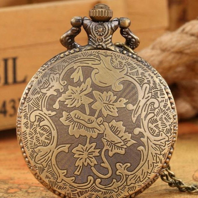 Close-up of an ornate, bronze-colored pocket watch with floral and bird designs, set against a blurred backdrop.