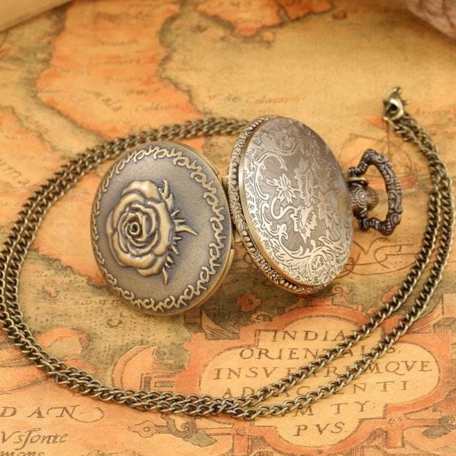 Open antique bronze pocket watch with a rose design on its cover rests on a chain over a map.