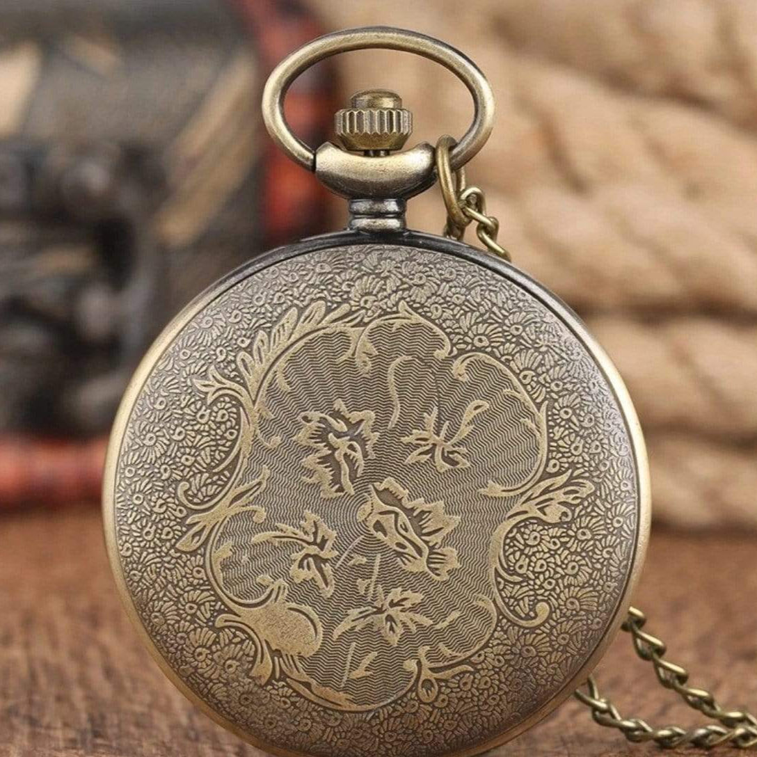 Close-up of an ornate, bronze-toned pocket watch on a wooden surface.