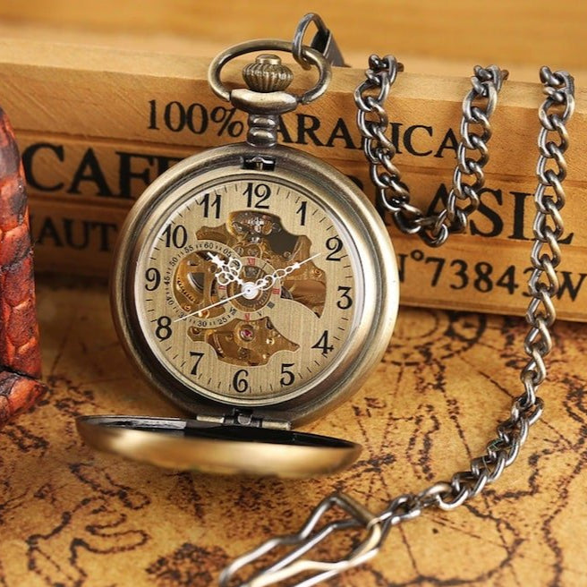Antique-style bronze pocket watch with open face, attached to a chain, lying on a map.