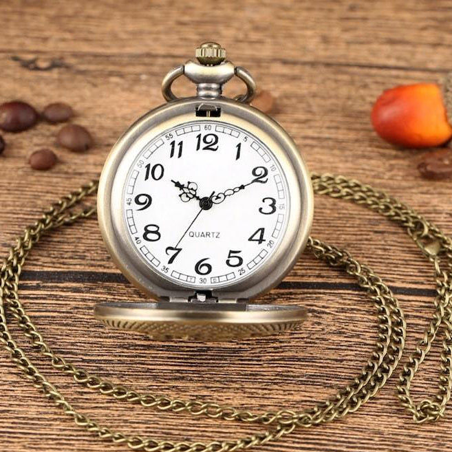 Vintage pocket watch with a brass chain, on a wooden surface with an open lid, the watch face shows a white background with black numbers and hands.