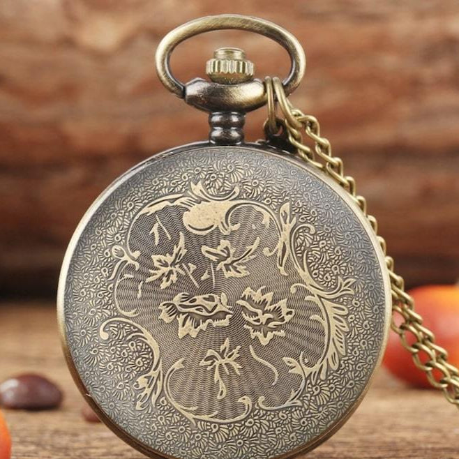 Bronze floral-engraved pocket watch with chain on wood surface.
