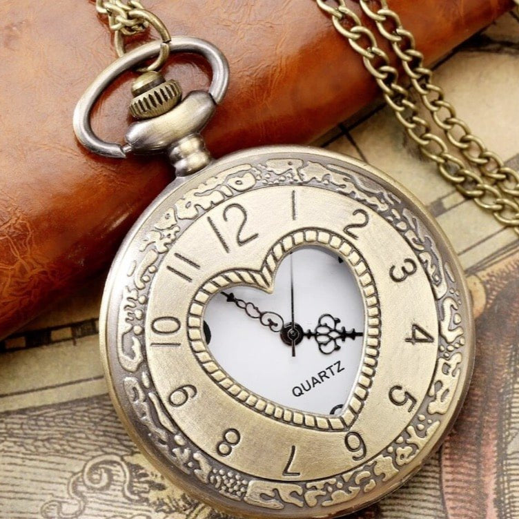 Close-up of an antique-gold heart-shaped pocket watch on a chain, displaying the time.