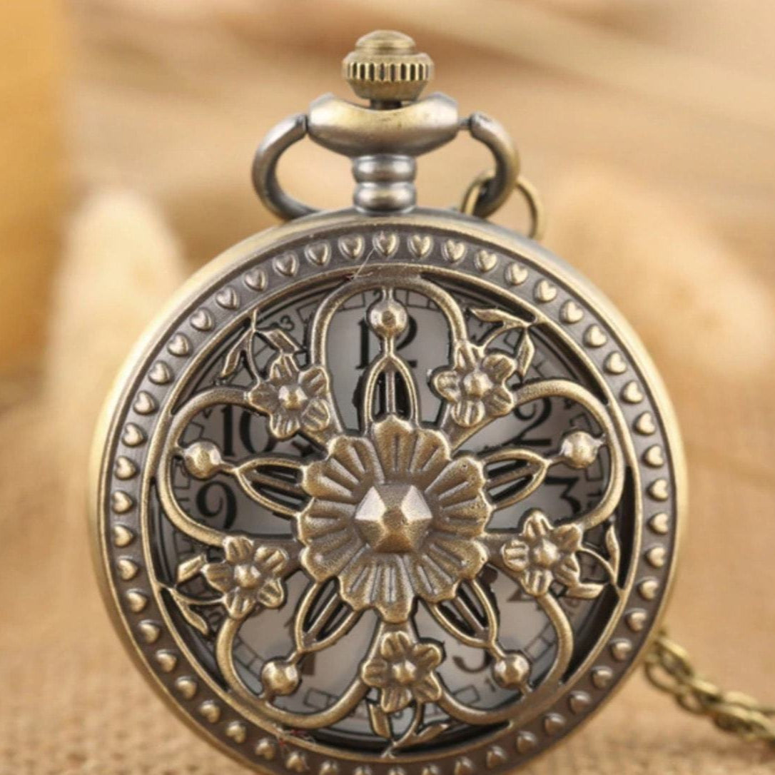 Close-up of an ornate, antique-style pocket watch with a floral design on its face and a chain attached.
