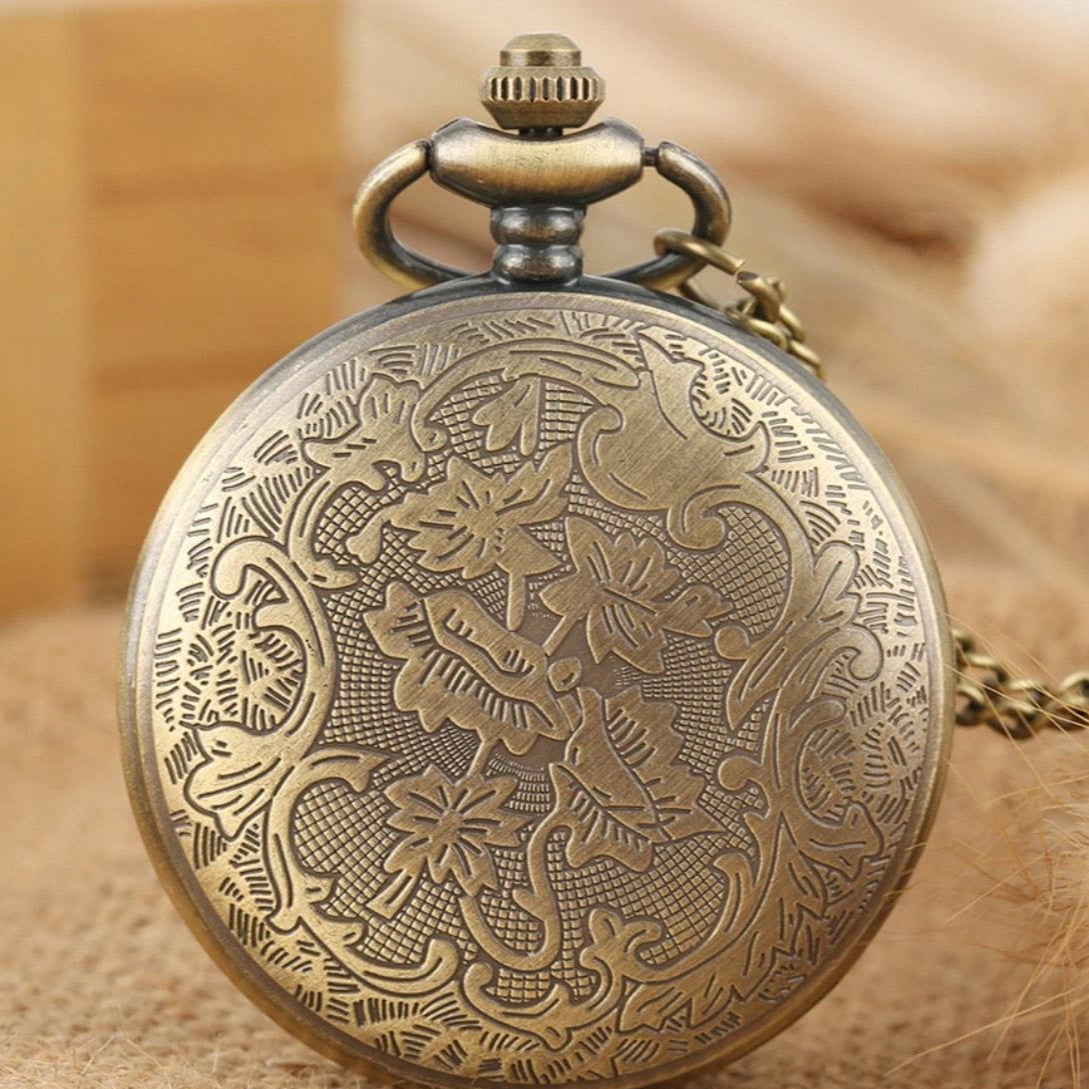 Close-up of an ornate, antique bronze pocket watch with a floral and scrollwork design.