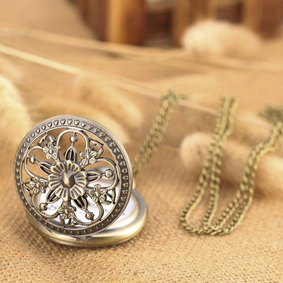 Close-up of an antique brass pocket watch with a floral design on its open lid and a matching chain lying on a burlap surface.