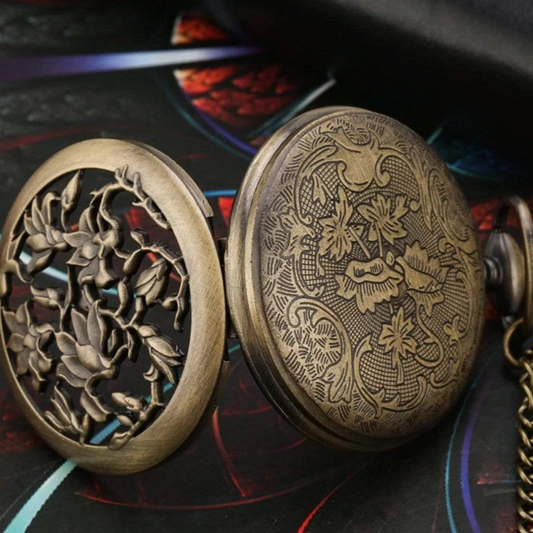 Open bronze pocket watch with floral cut-out and engraved lid.
