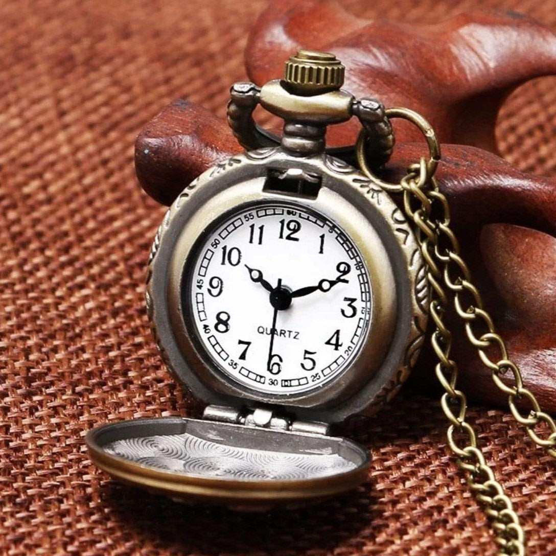 Close-up of an antique pocket watch with an open lid, gold chain, and brown wooden background.