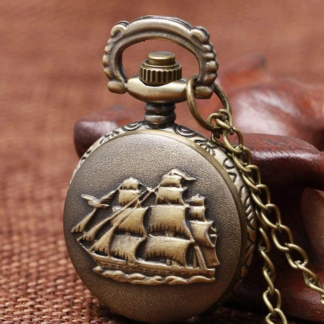 Close-up of a bronze pocket watch with a raised ship design and chain.