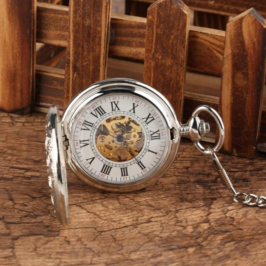 Silver pocket watch with a visible gear mechanism on a wooden surface.