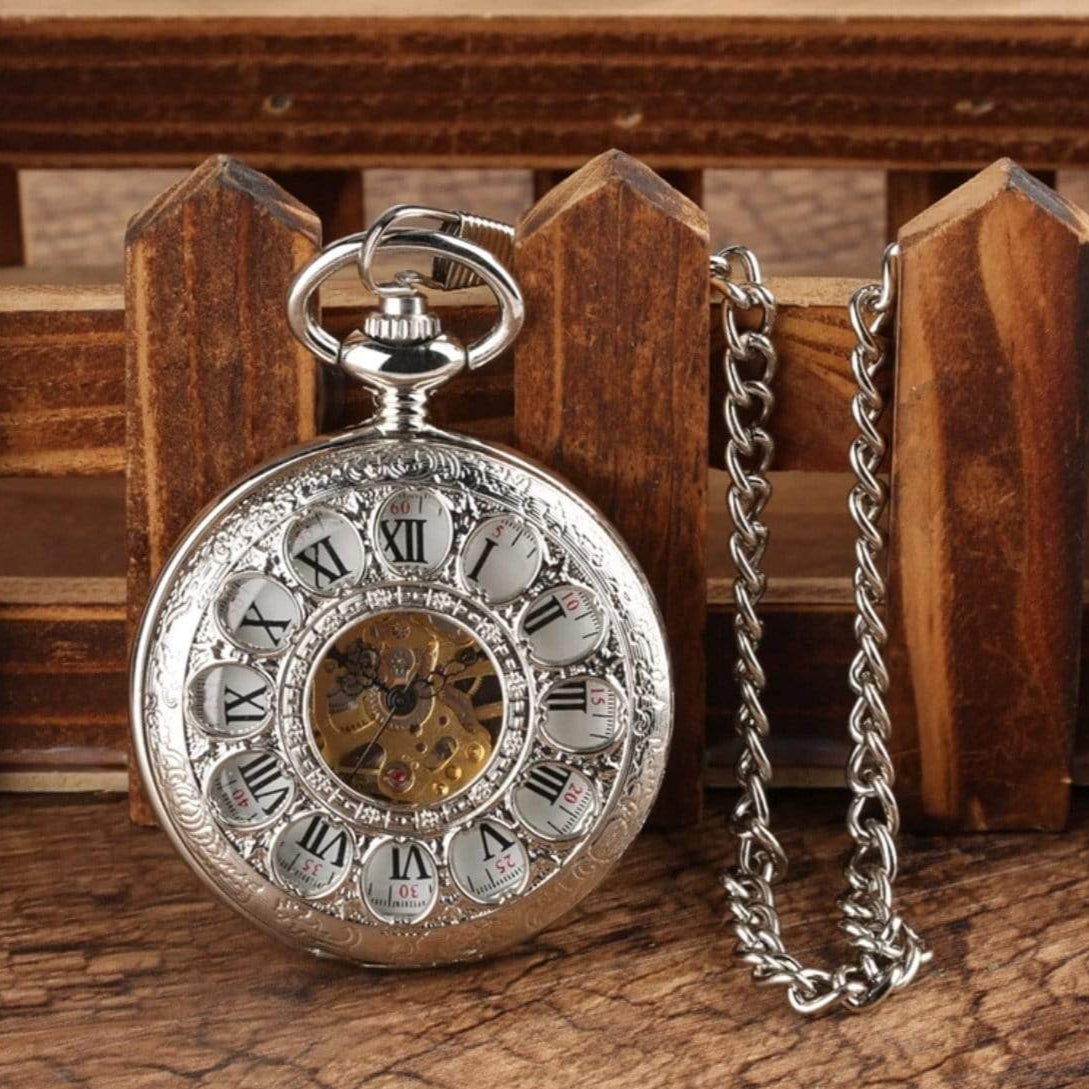 Silver pocket watch with chain on wood surface.
