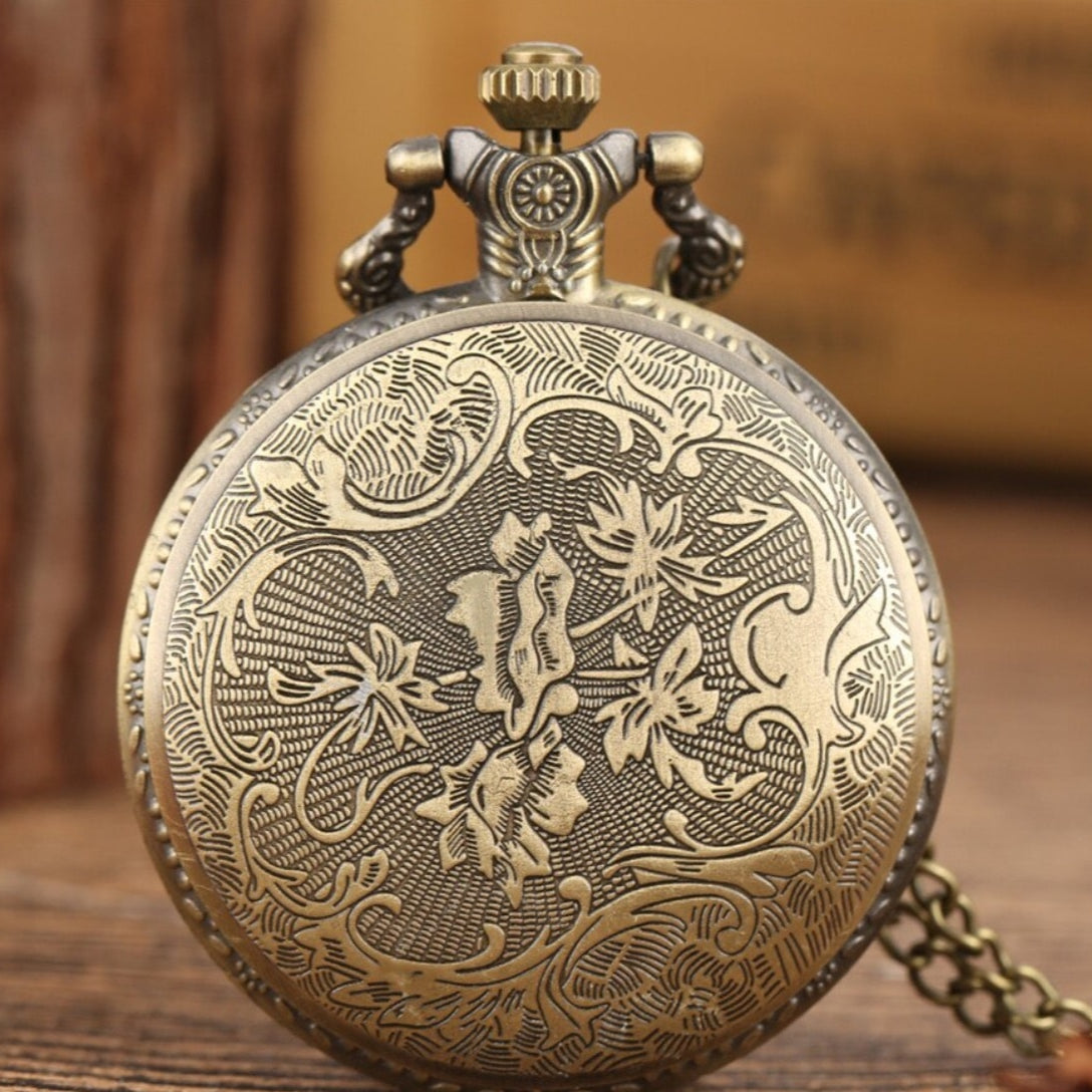 Close-up of an antique-style gold pocket watch with floral engravings on a wooden surface.
