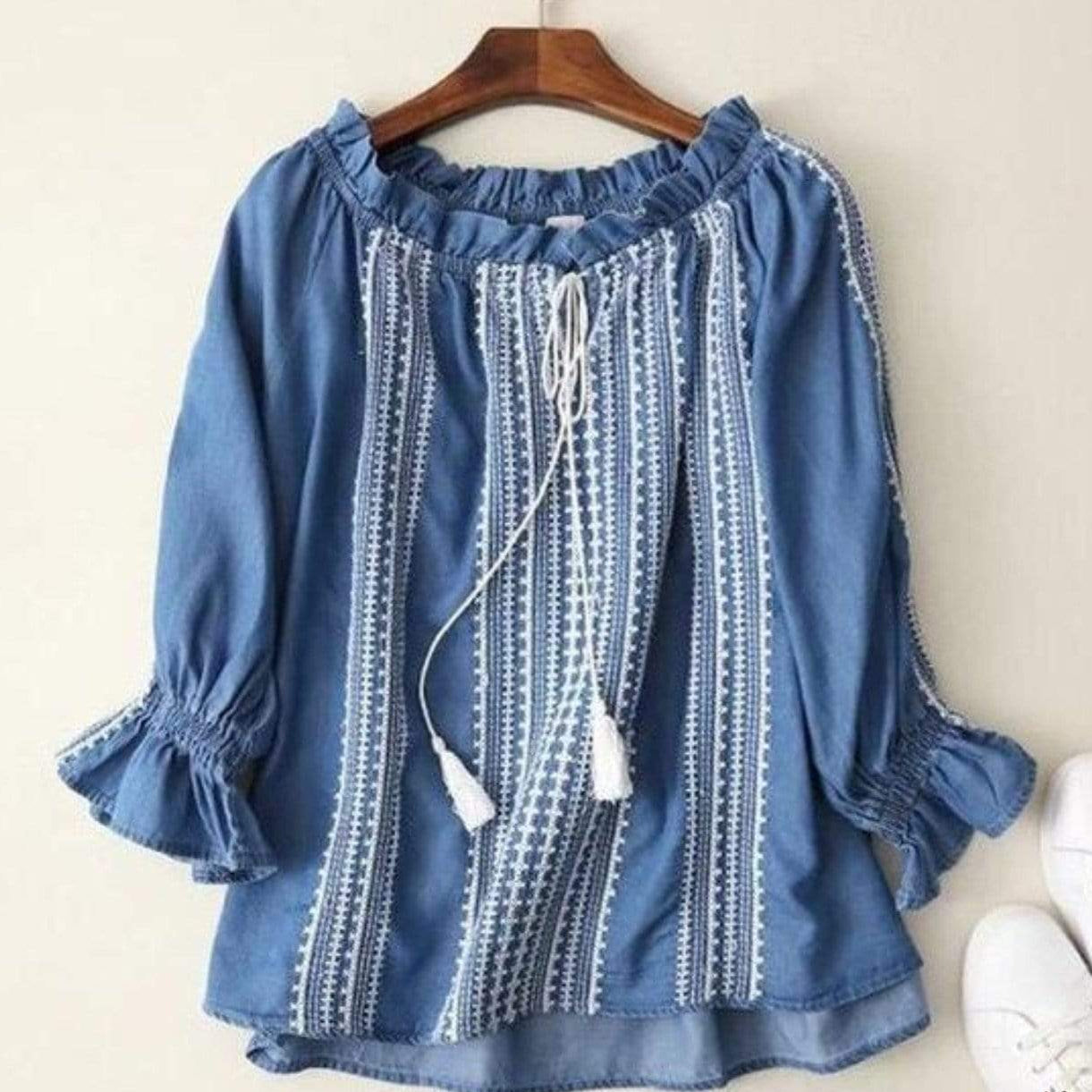Blue denim blouse with white embroidery, long sleeves, and drawstring closure.