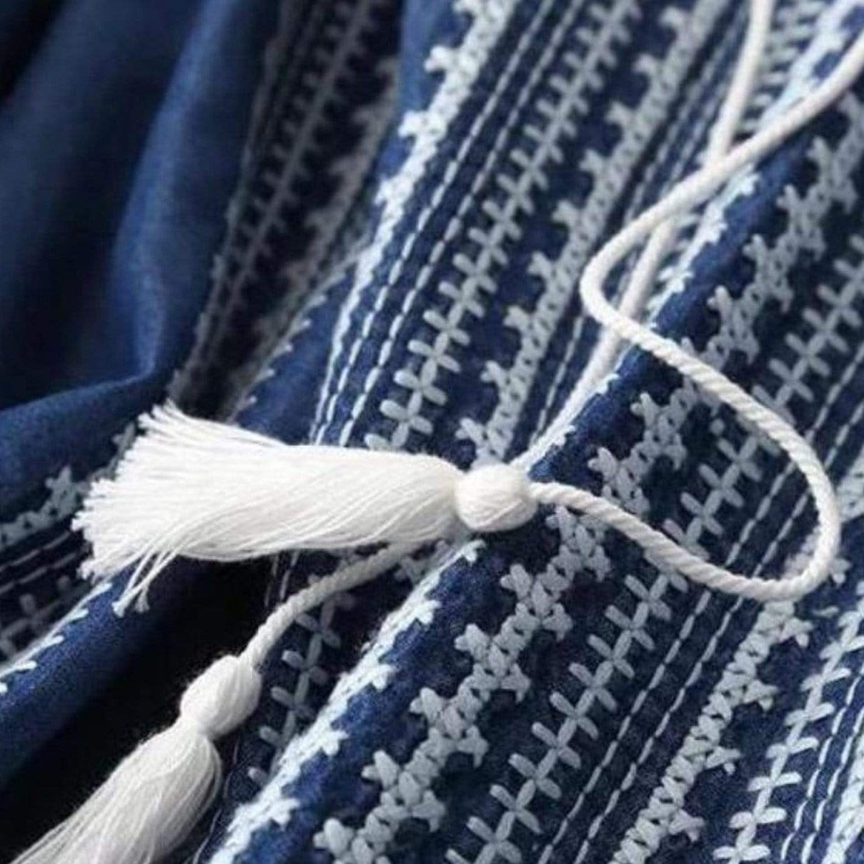 Close-up of blue and white embroidered fabric with white tassel.