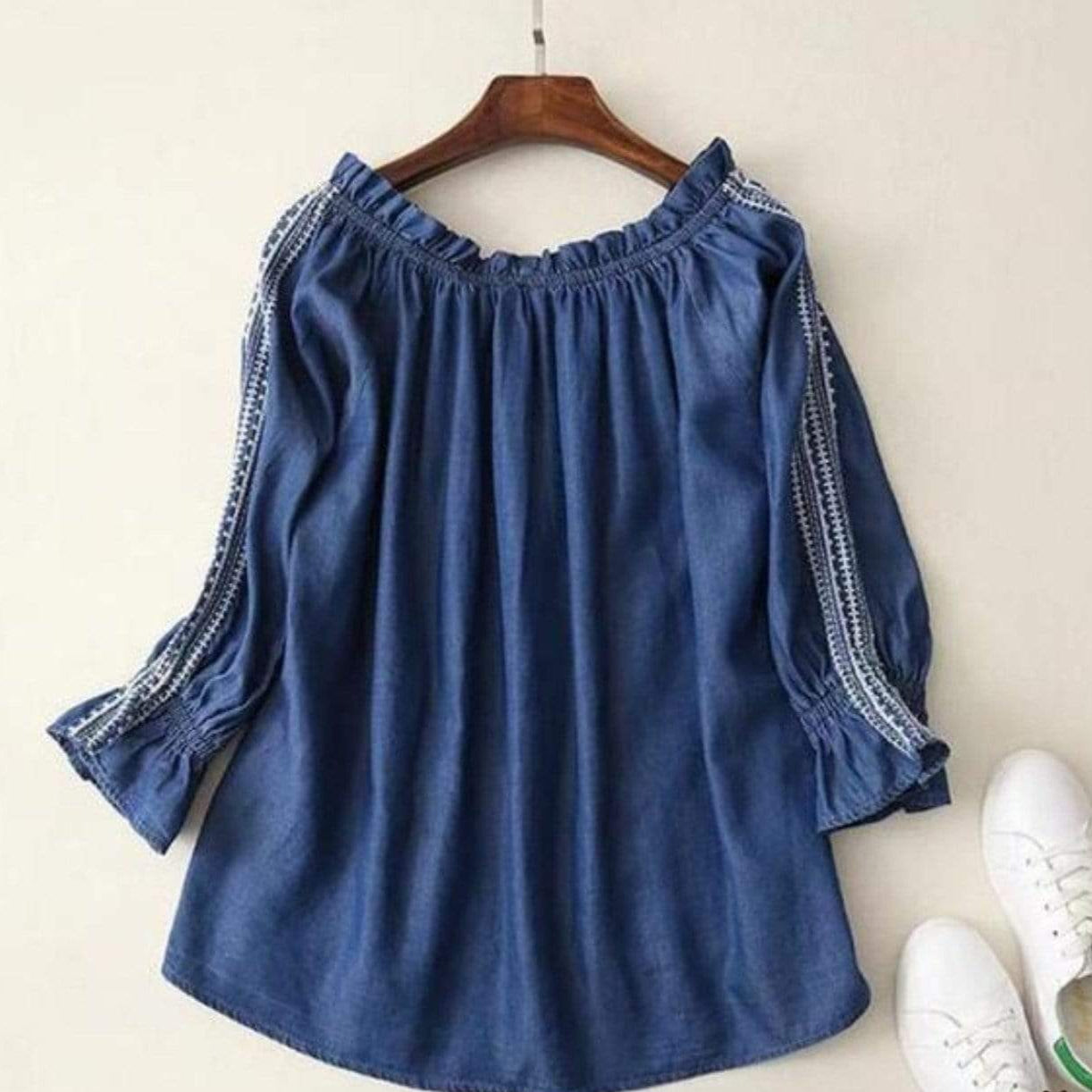 Blue off-the-shoulder blouse with embroidered sleeves, hanging above two white sneakers.
